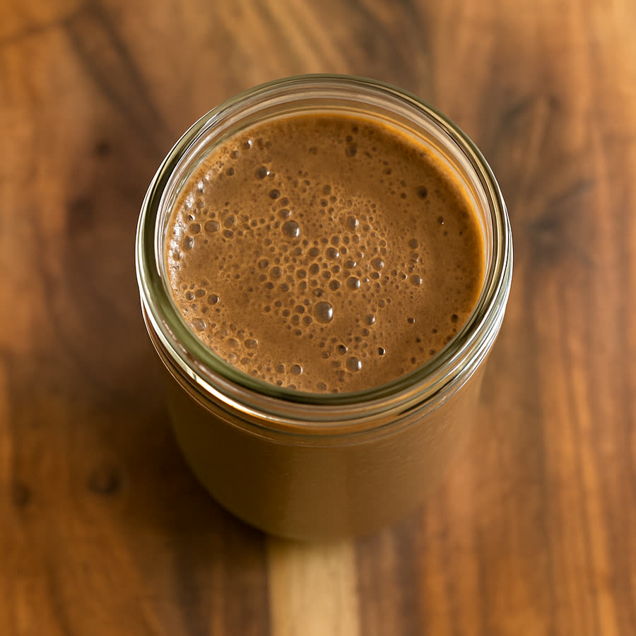A jar of chocolate XS protein shake on a wood table