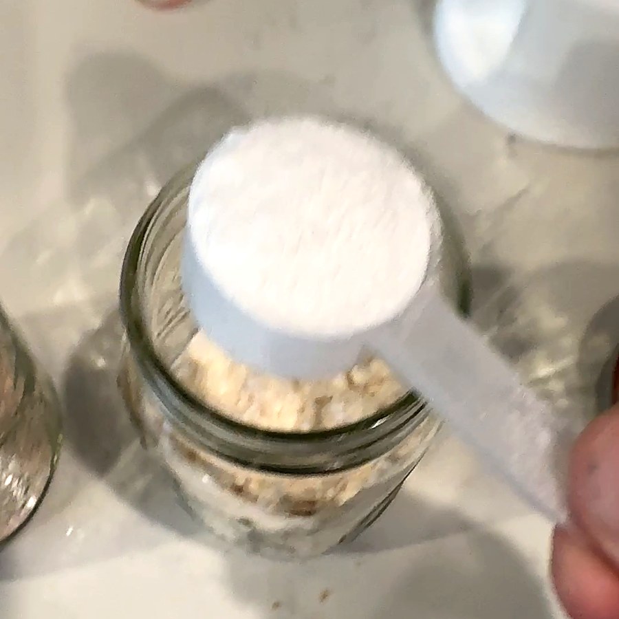 A scoop of creatine going into a mason jar of overnight oats