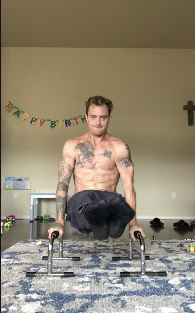 L-sit on parallettes in the living room, kids' toys on the floor, training at home with the kids around